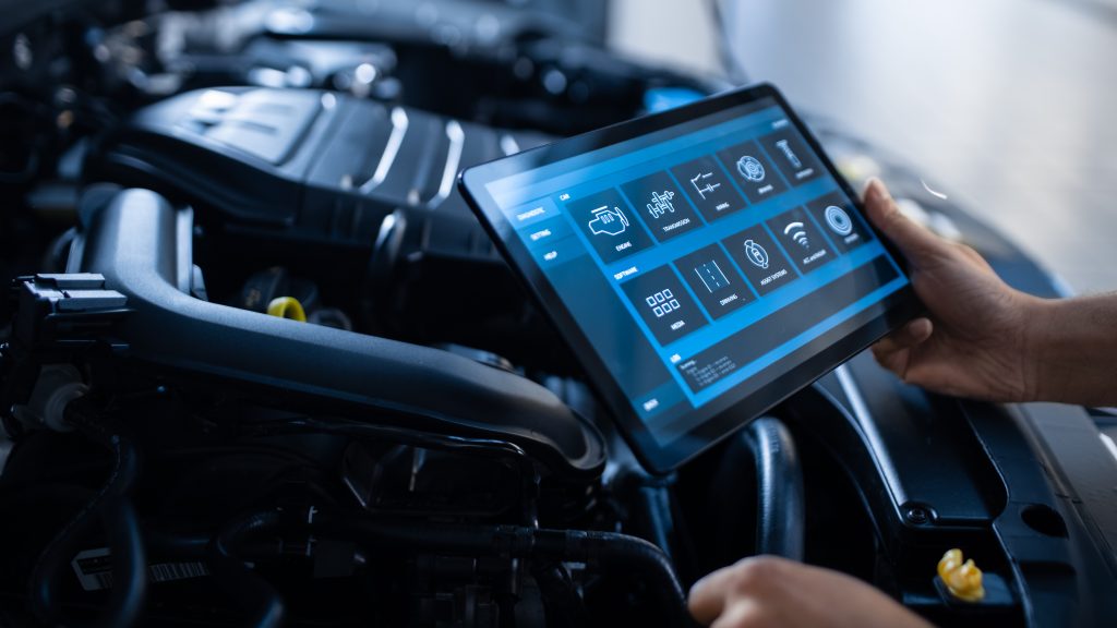 Personne utilisant une tablette de diagnostic au-dessus du moteur d’un véhicule dans un atelier automobile.